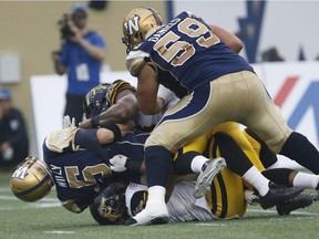 Hamilton Tiger-Cats' Taylor Reed (44) and Adrian Tracy (93) sack Winnipeg Blue Bombers' quarterback Drew Willy (5) during which he sustained an injury and was taken off during the first half of CFL action in Winnipeg Thursday, July 2, 2015.