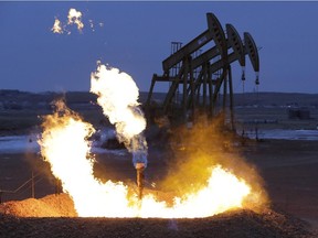 Oil pump jacks work behind a natural gas flare.