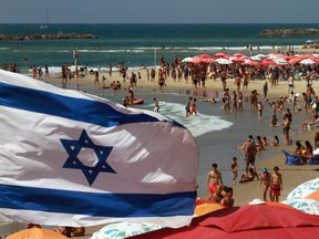 An Israeli flag flutters above umbrellas on the beach in the Mediterranean city of Tel Aviv.