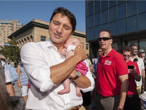Liberal Leader Justin Trudeau, left, holds baby Adalyn Hayes while Erika Golem, right, laughs during a campaign visit to the Regina Farmers' Market in Regina on Wednesday, August 12, 2015.