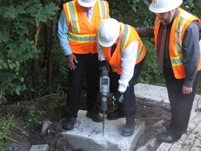 Montreal Mayor Denis Coderre, centre, uses a jackhammer to destroy a concrete foundation laid for an unauthorized community mailbox at the entrance to L'Anse-à-l'Orme Nature Parkin Pierrefonds-Roxboro on Thursday, Aug. 13, 2015.