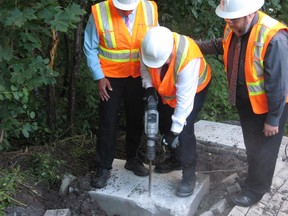 Montreal Mayor Denis Coderre, centre, uses a jackhammer to destroy a concrete foundation laid for an unauthorized community mailbox at the entrance to Anse-a-l'Orme Nature Park, in Montreal, on Thursday, Aug. 13, 2015.