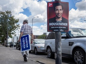 MONTREAL, QUE.: AUGUST 12, 2015 -- Nathan Elbert carries campaign signs for Conservative federal election candidate Robert Libman as he walks past a Liberal campaign sign for candidate Anthony Housefather on Decarie boulevard in the riding of Mount-Royal in Montreal on Wednesday, August 12, 2015. (Dario Ayala / Montreal Gazette)