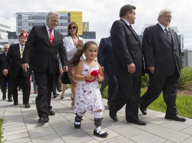 Shriners Hospital patient Marie-Pierre Paquette, holding a bow from a ribbon-cutting ceremony she took part in, leads dignitaries towards a dedication ceremony for the opening  of the new $127-million Shriners Hospital for Children Thursday, August 20, 2015. From the are: Jerry Gant, Imperial Potentate Shriners International, Quebec premier Philippe Couillard, Quebec Minister of Immigration, Diversity and Inclusiveness from Notre-Dame-de-Grâce Kathleen Weil, Montreal mayor Denis Coderre, and Gaétan Barrette,  Quebec health minister.