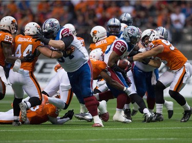 Montreal Alouettes' Tyrell Sutton (20) carries the ball through the line of scrimmage past B.C. Lions' Ryan Phillips, centre, and Craig Roh (93) during the first half of a CFL football game in Vancouver, B.C., on Thursday August 20, 2015.