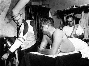 Twenty-one-year-old Jean Béliveau gets a rubdown and listens to Punch Imlach, his coach with the 1952-53  Quebec Aces of the Quebec Senior Hockey League.