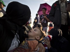 A Syrian child sleeps on his mother's lap as they wait with others to board a bus that will take them to the center for asylum seekers, after crossing the Serbian-Hungarian border near Roszke, southern Hungary,Sunday, Sept. 13, 2015.