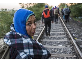 A woman looks back as migrants and refugees who arrived from Serbia walk on the track of the Horgos, Serbia, and Szeged, Hungary, railway line near the border village of Roszke, 180 kms southeast of Budapest, Hungary, during sunrise Wednesday, Sept. 9, 2015.