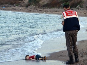 A paramilitary police officer investigates the scene before carrying the lifeless body of Alan Kurdi, 3, after a number of migrants died and a smaller number were reported missing after boats carrying them to the Greek island of Kos capsized, near the Turkish resort of Bodrum early Wednesday, Sept. 2, 2015.