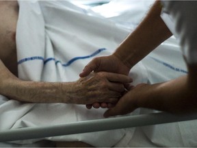 A nurse holds the hand of an elderly patient at a palliative care unit.