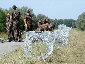 Hungarian soldiers set up razor wire, the first line of a temporary fence under construction on Hungary's southern border with Croatia destined to halt illegal migrants entering the country's territory from Croatia near Kolked, 215 kms south of Budapest, Hungary, Friday, Sept. 18, 2015. Hungary has begun to build a fence on the border with Croatia and will set up a "transit zone" near the village of Beremend where migrants entering from Croatia can request asylum.