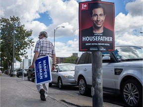 Man carries campaign signs for Conservative federal election candidate Robert Libman as he walks past a Liberal campaign sign for candidate Anthony Housefather.