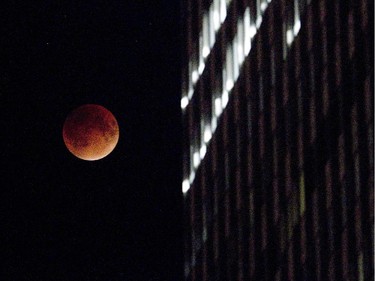 The perigee full moon, or "supermoon," appears red behind a downtown skyscraper in Montreal, Sunday, Sept. 27,  2015.