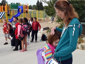 A Grade 2 student is comforted by her mom as she waits in the school yard for the bell to signal the start of school.