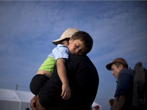 A migrant man holds his sleeping child as migrants and refugees queue to be registered at a camp after crossing the Macedonian-Greek border near Gevgelija on September 23, 2015. European Union leaders hold an emergency migration summit on September 23 amid a growing east-west split after ministers forced through a controversial deal to relocate 120,000 refugees.