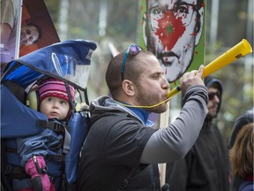 A protester carrying his young child blows a horn as thousands of protesters from a coalition of public sector unions march in the streets of Montreal Saturday, October 3, 2015. The protest included teachers, health workers and labour federation members against the Quebec government's latest contract offers.