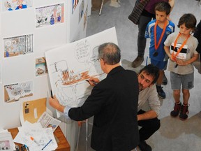 Le Devoir cartoonist Garnotte (Michel Garneau) draws a cartoon of Stephen Harper while another cartoonist Fleg (Christian Daigle) looks on.