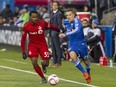 Montreal Impact coach Mauro Biello (rear in suit) watches a battle between his player Donny Toia (right) and Robbie Findley of Toronto FC in the first half of a game at Saputo stadium in Montreal Sunday, Oct. 25, 2015.