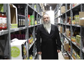 Rabbi Chaim Shlomo Cohen, executive director of the MADA community organization, stands between shelves filled with food.