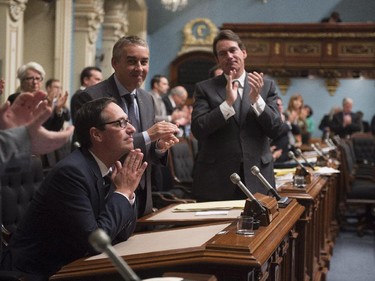 Quebec Opposition MNA Stephane Bedard, left, joins his hands after he announced his decision to resign, as Quebec Opposition Leader Pierre-Karl Peladeau, right, and members of the legislature applaud, Thursday, October 22, 2015 at the legislature in Quebec City.