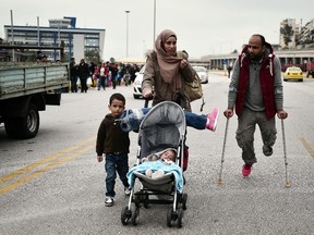 A Syrian man and his family look for transportation to central Athens or continue towards the Greek-Macedonian border from the port of Piraeus on October 21, 2015. His prosthetic leg is placed on his baby's stroller.