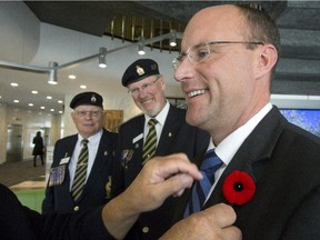 With fellow members of the Royal Canadian Legion Ross Seip (left) and Caspar Koevoets watching on, Norm Piche pins Mayo Matt Brown with the first poppy of the season in London, Ont. on Tuesday, October 27, 2015. The annual poppy campaign kicks off Friday, October 30.