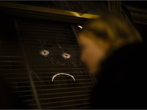 A woman walks past The Belle Équipe restaurant window showing two bullet holes and the shape of a sad mouth drawn underneath, in Paris, Saturday, Nov. 14, 2015, a day after the attacks on Paris. French President François Hollande vowed to attack Islamic State without mercy as the jihadist group admitted responsibility Saturday for orchestrating the deadliest attacks inflicted on France since the Second World War.