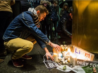 A man lights a candle as people gather in front of the French consulate in Montreal for a night-time vigil for the victims of the terrorist attack in France on Friday, November 13, 2015.