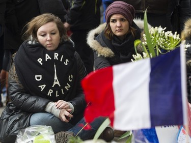 Women sit beside a makeshift memorial outside the French consulate in Montreal on Sunday, Nov. 15 , 2015, after a march in solidarity with Paris.