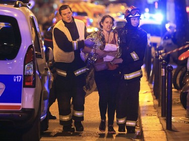 Rescue workers help a woman after a shooting, outside the Bataclan theater in Paris, Friday Nov. 13, 2015.  French President Francois Hollande declared a state of emergency and announced that he was closing the country's borders.