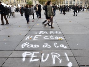 Parisians walk past graffiti after a minute of silence Nov. 16, 2015, in to pay tribute to victims of the attacks claimed by Islamic State, which killed at least 129 people and left more than 350 injured.