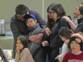 Joseph Gunner, left, uncle of police officer and fire victim Charlie Gunner, stands with other family members and friends of the five men who perished in a cabin fire in Mistissini, as the gather around photographs of the men at a memorial service in the Cree village north of Montreal, Friday April 3, 2015.  The five men from the village who perished earlier in the week were north of the village hunting.