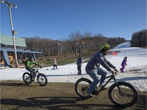 Mountain bikers on their fat tire bikes pass by a very lightly used ski hill and head to the bike trails at Mont Rigaud Ski Centre, in Rigaud, west of Montreal on Saturday, December 26, 2015.  Unseasonable warm weather has made it difficult for ski hills in the area to make snow, and keep it on the hills.