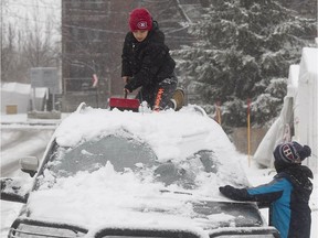 Eight year-old Adam Benzia, top, cleans the snow off the family car with his cousin Kenny Mihoubi. Adam wants to surprise his mother following the first significant snowfall of the season to hit Montreal on Sunday December 27, 2015.