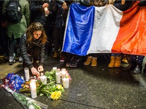 A woman lights a candle as people gather in front of the French consulate in Montreal for a night-time vigil for the victims of the terrorist attack in France on Friday, November 13, 2015.