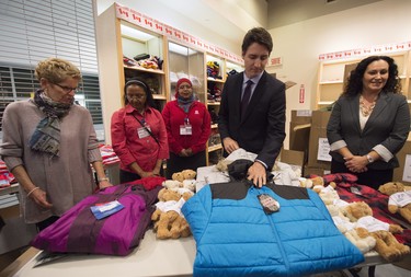 Canadian Prime Minister Justin Trudeau, second right, and Ontario Premier Kathleen Wynne, left, over look winter wear that will be handed out before they greet refugees from Syria at Pearson International airport, in Toronto, on Thursday, Dec. 10, 2015.