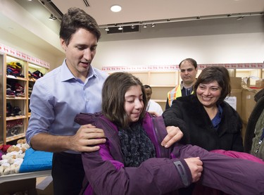 Canadian Prime Minister Justin Trudeau gives newly-arrived Syrian refugee Sylvie Garabedian, centre, a winter jacket as her mother Anjilik Jaghlassian, right, looks on at Pearson International airport, in Toronto, on Friday, Dec. 11, 2015.