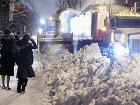 Two tourists take pictures as a snow removal crew clears the streets in the Mile End district of Montreal on Sunday Jan. 3, 2016.