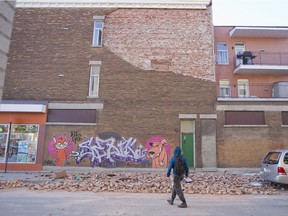 A pedestrian walks past bricks from a partially collapsed exterior wall on Dorion St. at the corner of Ontario St. in Montreal, Jan. 11, 2016, following strong winds overnight.