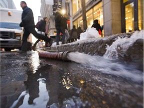 A man jumps over a hose draining water from a broken water main at the corner of Peel and Ste. Catherine Sts. in Montreal Monday, January 4, 2016.