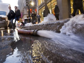 People walk over a hose draining water from a broken water main at the corner of Peel and Ste-Catherine Sts. in Montreal Monday, January 4, 2016.