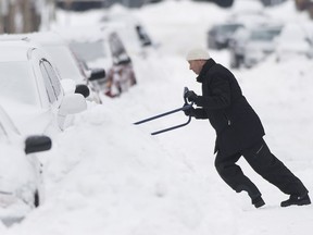 A man clears snow from around his car in Montreal Wednesday, December 30, 2015 following the first major storm of winter in the region.