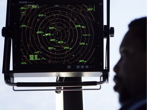 An air traffic controller stands beneath a radar screen.