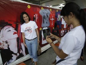 A Filipino fan has her picture taken beside a poster of Madonna before they go inside the venue where she will be holding a concert in suburban Pasay, south of Manila, Philippines on Wednesday, Feb. 24, 2016. Pop star Madonna made a surprise visit to two Manila shelters for orphans and street children, taking selfies with kids a day before the start of her two-night concert stint in the Philippine capital. (AP Photo/Aaron Favila)