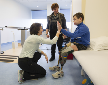 hysiotherapist Rochelle Rein and Mykola Nyzhnykovskyi 'high-five' as Mykola's mother Alla Nyzhnykovska looks on at Shriners Hospitals for Children in Montreal Tuesday, March 15, 2016. Mykola lost his legs and an arm in East Ukraine and sustained other serious injuries from an exploding grenade that killed his younger brother.