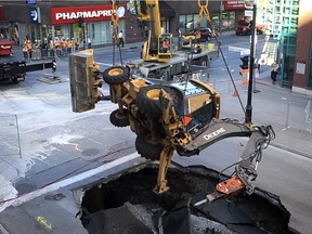 A crane company employee attaches chains to backhoe that fell into a sinkhole the previous day on St. Catherine St. at Guy in Montreal Tuesday August 6, 2013.