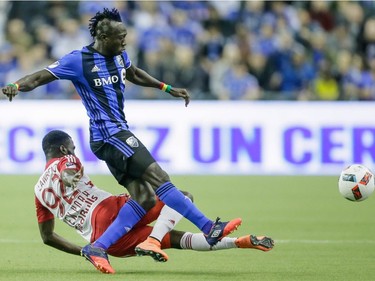Montreal Impact forward Dominic Oduro, standing, passes the ball as he is tackled by New York Red Bulls defender Kemar Lawrence during the first half of the Impact's home opening match at the Olympic Stadium in Montreal on Saturday, March 12, 2016.
