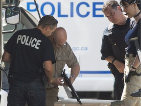 Montreal police officers look at a weapon seized from a house in Montreal, Wednesday, July 31, 2013, following a standoff with an armed man.