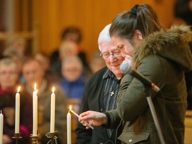Alexandra Lapierre, right, daughter of Louis Lapierre, and priest Rejean Coulombe, left, light a candle during a commemorative mass for the victims of the March 29 airplane crash at Sainte-Madeleine de Havre-aux-Maisons church in Les Iles de la Madeleine on Tuesday, April 5, 2016.