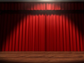A regular theater stage with closed red curtains lit by a single spotlight.